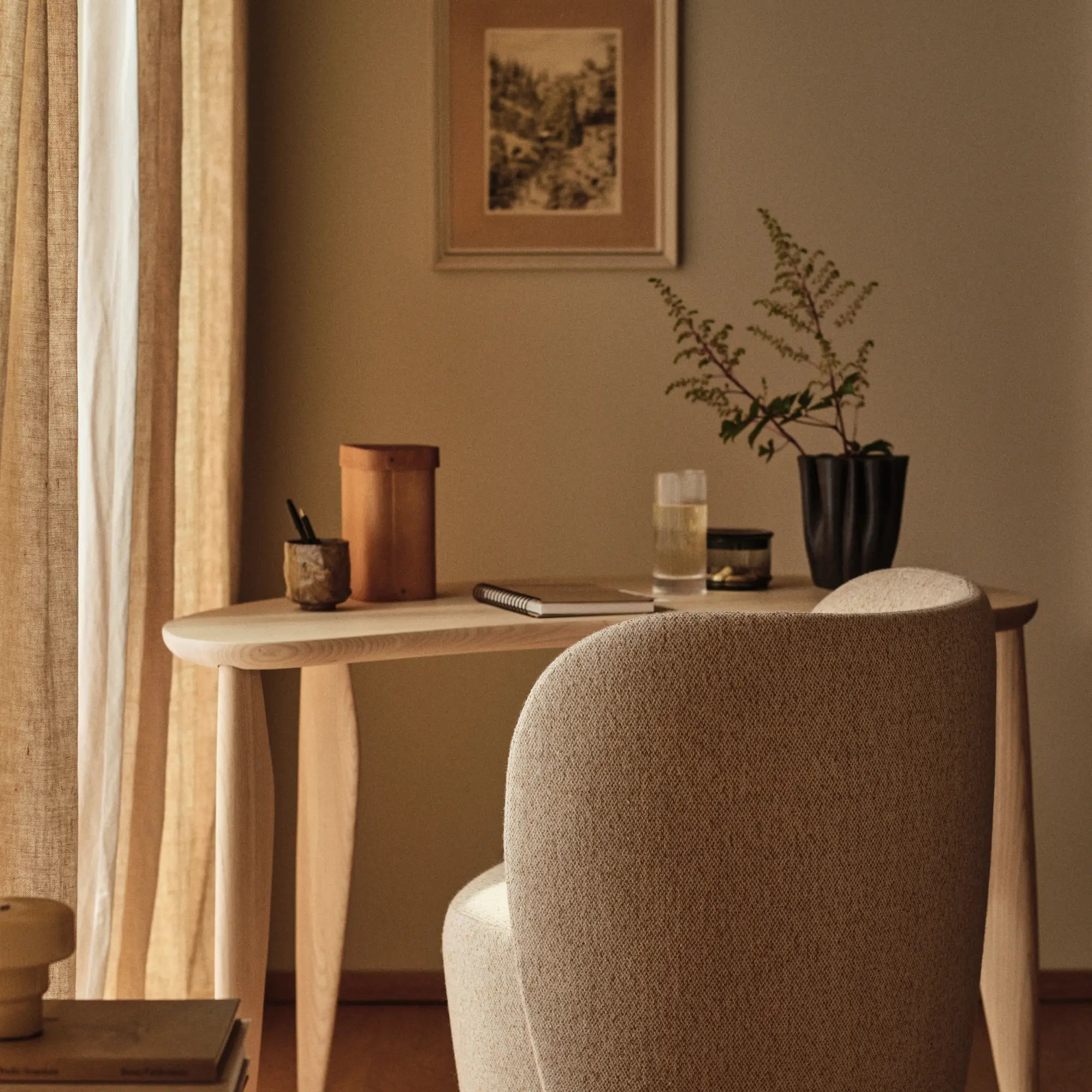 Slankt konsolbord brugt som skrivebord ved et vindue med en rund lænestol og sort vase