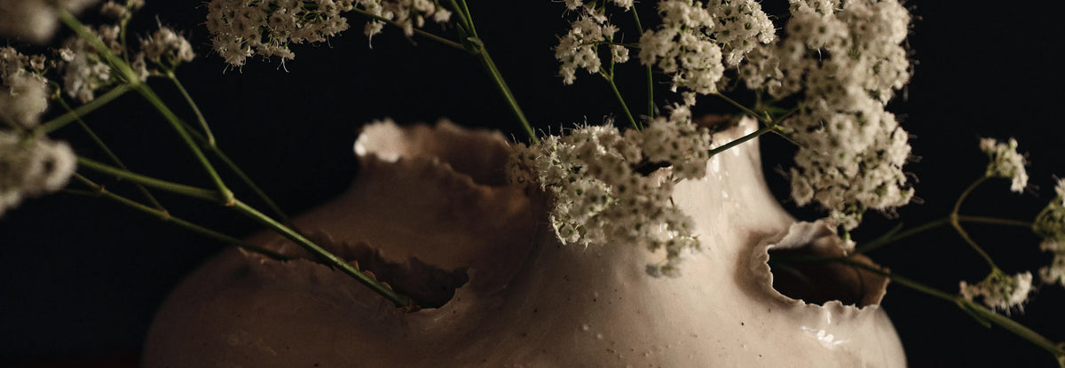De sidste detaljer, nærbillede af en off-white vase med flossede åbninger og små hvide blomster
