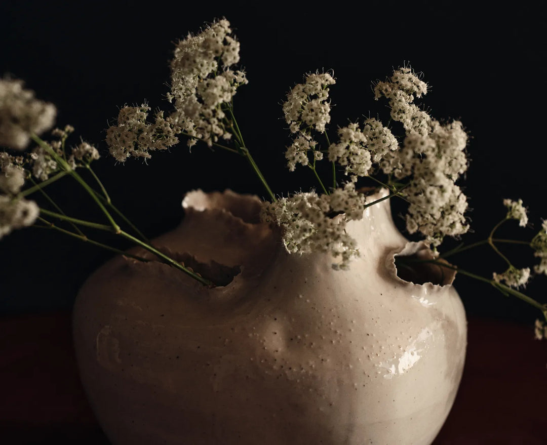 De sidste detaljer, nærbillede af en off-white vase med flossede åbninger og små hvide blomster