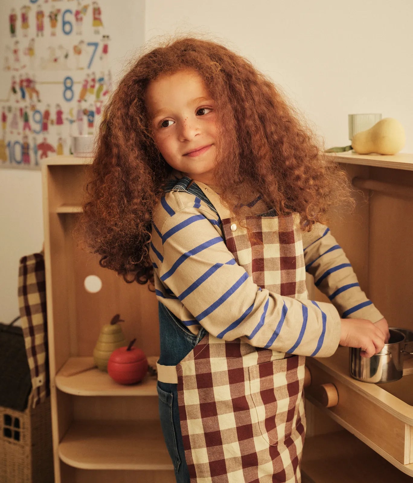 Kids Autumn Winter 2026, barn i ternet forklæde med en gryde ved et legekøkken, legetøjsfrugt på hylden